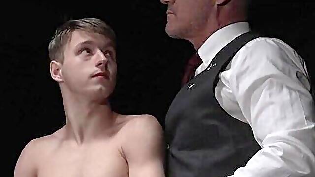 Beefy man in a suit is examining a shy blond fellow